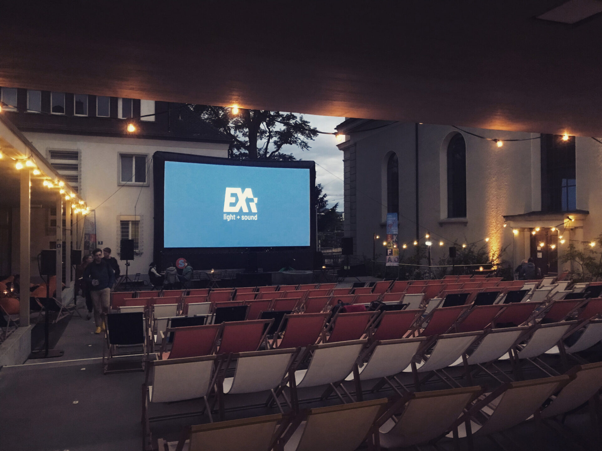 Leinwand mit Exa Light & Sound Logo for Liegestühlen im Hof des Sofaopenairkino Wipkingen